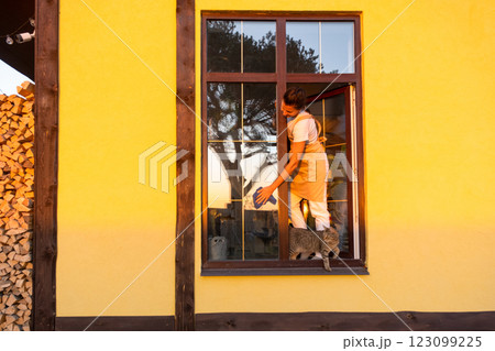 Woman in apron manually washes the window of the house with a rag with a spray cleaner and a mop outside. Safety at height, restoring order and cleanliness in the spring, cleaning service 123099225