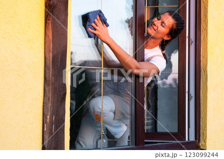 Woman in apron manually washes the window of the house with a rag with a spray cleaner and a mop outside. Safety at height, restoring order and cleanliness in the spring, cleaning service Woman in apron manually washes the window of the house with a rag with a spray cleaner and a mop outside. Safety at height, restoring order and cleanliness in the spring, cleaning service 123099244