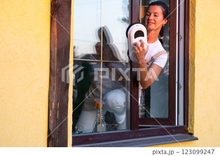 A woman launches window cleaner robot of house outside with a yellow facade. Household robotics, household assistant, cleaning servise 123099247
