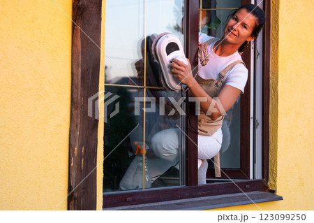 A woman launches window cleaner robot of house outside with a yellow facade. Household robotics, household assistant, cleaning servise 123099250