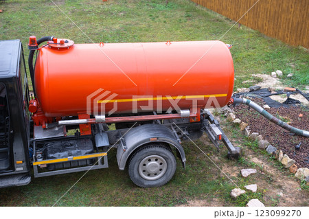 The orange tank of the sewage disposal machine in the courtyard of the house sucks sewage waste from the septic tank well. Waste disposal service, sewage disposal The orange tank of the sewage disposal machine in the courtyard of the house sucks sewage waste from the septic tank well. Waste disposal service, sewage disposal 123099270
