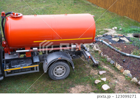 The orange tank of the sewage disposal machine in the courtyard of the house sucks sewage waste from the septic tank well. Waste disposal service, sewage disposal The orange tank of the sewage disposal machine in the courtyard of the house sucks sewage waste from the septic tank well. Waste disposal service, sewage disposal 123099271