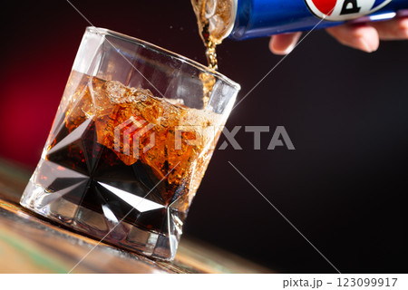 Cola is poured into a glass with ice cubes on a dark background close-up Cola is poured into a glass with ice cubes on a dark background close-up 123099917