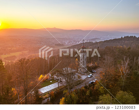 The lookout tower stands majestically on Prosec Ridge, offering stunning autumn views of Jablonec nad Nisou as the sun sets over the Jizera Mountains, painting the sky in warm hues. 123100083