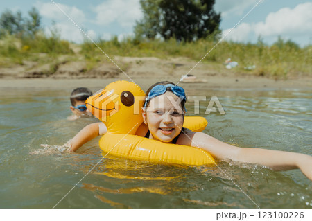 Children playing in a lake with an inflatable duck ring on a sunny day. Fun summer day: boy teasing his sister while swimming in the lake Children playing in a lake with an inflatable duck ring on a sunny day. Fun summer day: boy teasing his sister while swimming in the lake 123100226