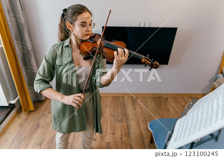 Young girl student playing violin and learning musical composition from sheet music. A young musician refines her skills through focused classical music practice. 123100245