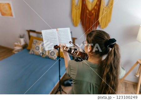 Young woman playing violin at home by sheet music, focused on learning music. Violin student rehearsing classical music in a professional study session Young woman playing violin at home by sheet music, focused on learning music. Violin student rehearsing classical music in a professional study session 123100249