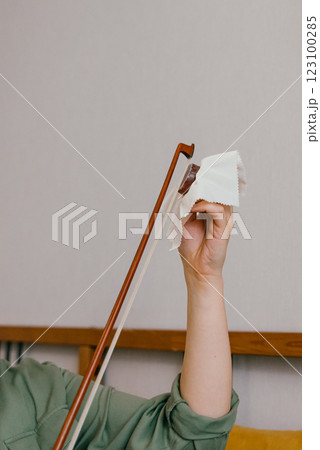 A woman's hand rubbing the bow with rosin at home, close-up. Violinist preparing her bow for practice with careful maintenance 123100285