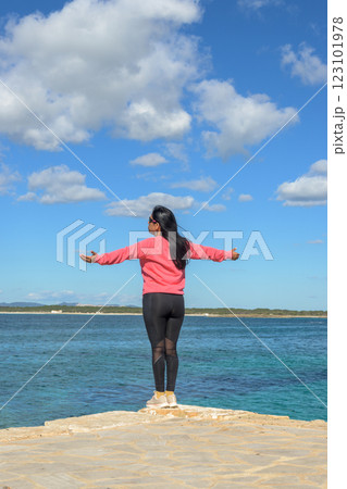 A latin woman stands with her arms open wide, facing the ocean and enjoying the serene view A latin woman stands with her arms open wide, facing the ocean and enjoying the serene view 123101978