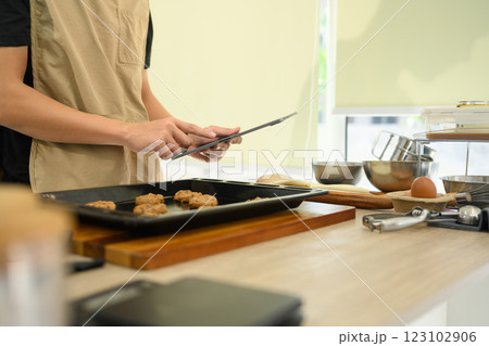 Young man preparing chocolate chip cookies in the kitchen and following recipe on digital tablet Young man preparing chocolate chip cookies in the kitchen and following recipe on digital tablet 123102906