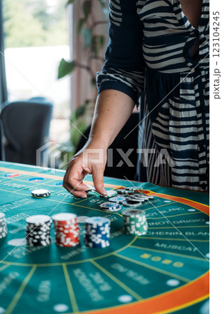 Hand placing a poker chip on a wine-themed casino game mat, blending gambling and wine culture for a unique entertainment experience Hand placing a poker chip on a wine-themed casino game mat, blending gambling and wine culture for a unique entertainment experience 123104245
