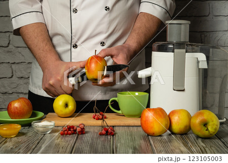 A skilled chef is carefully peeling a red apple, surrounded by fresh fruits and a juicer on the wooden countertop. The warm ambiance creates a welcoming cooking atmosphere A skilled chef is carefully peeling a red apple, surrounded by fresh fruits and a juicer on the wooden countertop. The warm ambiance creates a welcoming cooking atmosphere 123105003