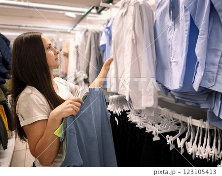 A young woman with long dark hair is choosing clothes for a child in a store 123105413