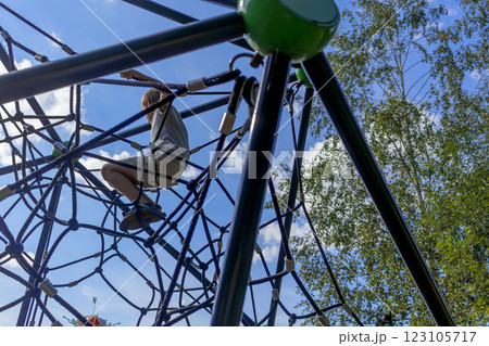 Boy sitting on rope web on playground against sky. Children's games in fresh air 123105717