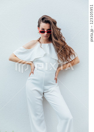 Beautiful brunette woman in white suit posing by the wall with plants Beautiful brunette woman in white suit posing by the wall with plants 123105951