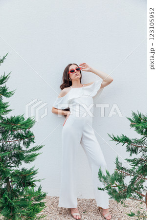 Beautiful brunette woman in white suit posing by the wall with plants 123105952