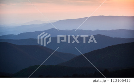 Tranquil scene at dusk, showcasing layers of rolling hills bathed in soft blue hues, with fading light of sunset casting gentle orange and pink glow over distant horizon. Tranquil scene at dusk, showcasing layers of rolling hills bathed in soft blue hues, with fading light of sunset casting gentle orange and pink glow over distant horizon. 123106413