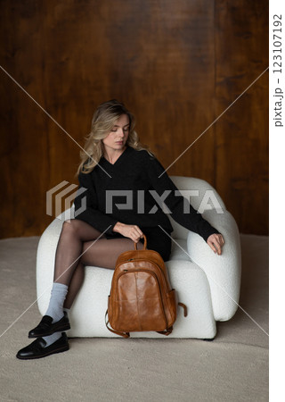 A girl in a warm sweater, a black short skirt, nylon tights, and black shoes is posing with a brown backpack. A girl in a warm sweater, a black short skirt, nylon tights, and black shoes is posing with a brown backpack. 123107192