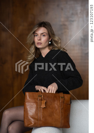 A girl in a warm sweater, a black short skirt, nylon tights, and black shoes is posing with a brown bag. A girl in a warm sweater, a black short skirt, nylon tights, and black shoes is posing with a brown bag. 123107193