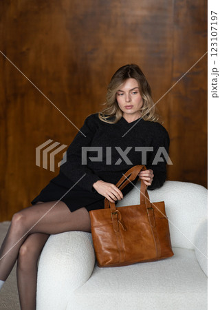 A girl in a warm sweater, a black short skirt, nylon tights, and black shoes is posing with a brown bag. A girl in a warm sweater, a black short skirt, nylon tights, and black shoes is posing with a brown bag. 123107197