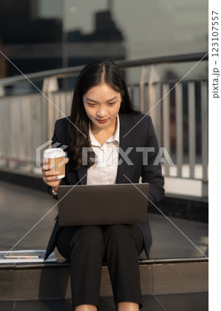 Happy business woman using computer iin front of a modern office building. Stylish woman manager smiling, working on financial and marketing projects. 123107557