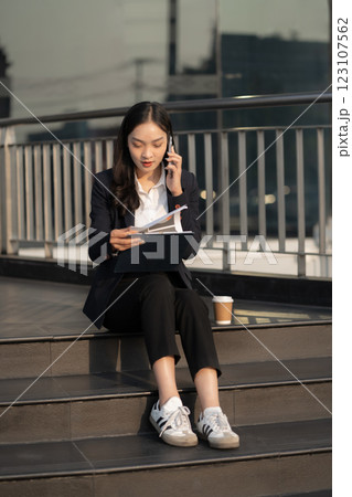 Businesswoman talks on phone, updates tasks, and plans milestones on a laptop. Online business, technology, in front of a modern office building. Businesswoman talks on phone, updates tasks, and plans milestones on a laptop. Online business, technology, in front of a modern office building. 123107562