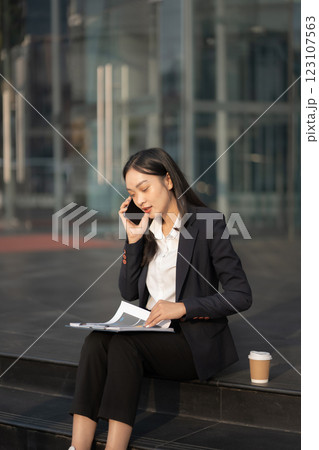 Businesswoman talks on phone, updates tasks, and plans milestones on a laptop. Online business, technology, in front of a modern office building. Businesswoman talks on phone, updates tasks, and plans milestones on a laptop. Online business, technology, in front of a modern office building. 123107563