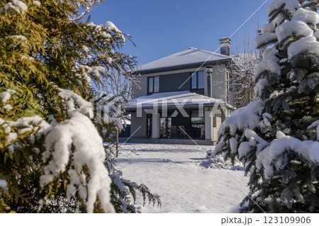 Modern two-story house in a winter landscape, surrounded by snow-covered evergreen trees under a clear blue sky. Modern two-story house in a winter landscape, surrounded by snow-covered evergreen trees under a clear blue sky. 123109906