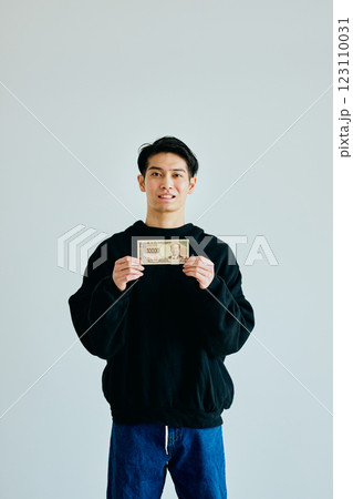 一万円札を持つ20代の若い男性 123110031