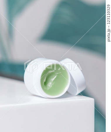 Opened white blank lip balm jar on wash basin in green tropical bathroom close up, cosmetic mockup 123110329