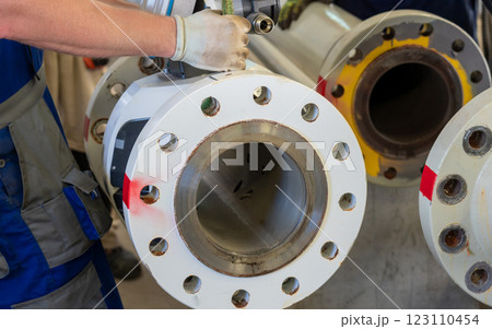 Worker dismantling an ultrasonic flowmeter from a flanged pipeline in an industrial setting. 123110454