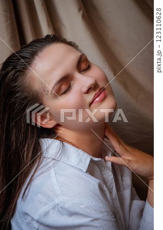 Portrait of a relaxed woman with a blissful expression in soft light. Caucasian woman with glitter on face. Beige background Portrait of a relaxed woman with a blissful expression in soft light. Caucasian woman with glitter on face. Beige background 123110628