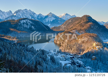 Serene Winter Alpine Valley with Snow-Capped Peaks, Reflective Lake, Evergreen Forest, and Quaint Village Under Golden Light Serene Winter Alpine Valley with Snow-Capped Peaks, Reflective Lake, Evergreen Forest, and Quaint Village Under Golden Light 123110726