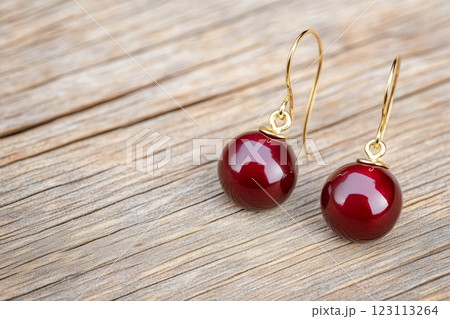 Vintage dark cherry earrings with gold accents on a wooden table evoke chic nostalgia 123113264