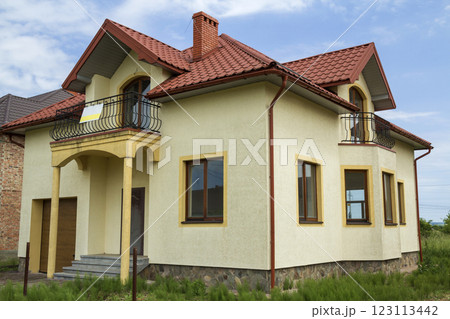 New yellow two-story residential cottage with shingle roof, front porch, plastic windows, high chimneys, balconies on blue sky background. Real estate property, architecture and prosperity concept. New yellow two-story residential cottage with shingle roof, front porch, plastic windows, high chimneys, balconies on blue sky background. Real estate property, architecture and prosperity concept. 123113442