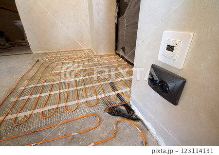 Heating red electrical cable wire system installed on cement floor in small new unfinished room with plastered walls. Renovation and construction, modern technology, comfortable warm home concept. 123114131