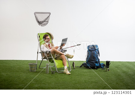 Businessman sitting on chair holding laptop and fishing rod while focused on screen against white studio background. Businessman sitting on chair holding laptop and fishing rod while focused on screen against white studio background. 123114301