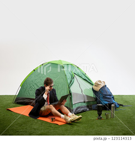 Businessman sitting on camping mat working on laptop while talking on phone against white studio background. 123114313
