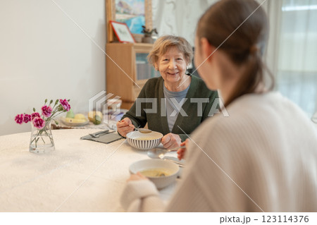 Senior woman enjoying meal with younger female family member at home. Concept of family bonding, aging, and healthy eating. Grandmother spending quality time with granddaugther at home.  123114376