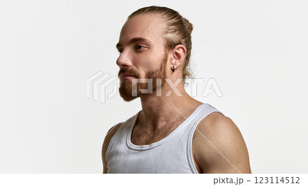 Man with tied-back hair and beard in white tank top, looking straight, showcasing masculine elegance against white studio background. 123114512