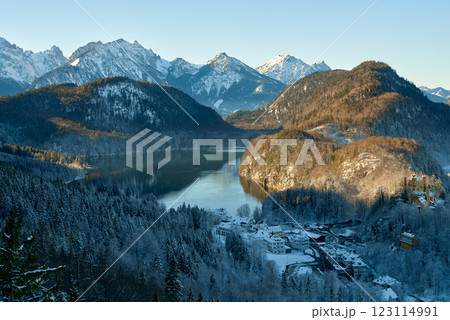 Picturesque Snowy Village by Reflective Lake in Alpine Valley with Majestic Snow-Capped Mountains and Evergreen Forest Under Clear Blue Sky Picturesque Snowy Village by Reflective Lake in Alpine Valley with Majestic Snow-Capped Mountains and Evergreen Forest Under Clear Blue Sky 123114991