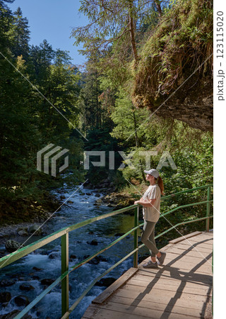 Stunning Young Woman Enjoying Scenic Mountain River View on a Hiking Trail in the Alps During Summer. Idyllic Alpine Landscape Captures the Essence of Outdoor Adventure and Natural Beauty. 123115020