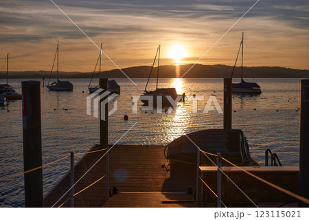 A serene sunset over a calm river, with vibrant orange and pink hues in the sky. A small sailboat is anchored in the water, reflecting the colorful sky. 123115021