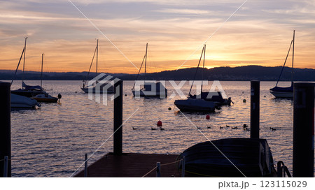 Pier at Sunset with Sailboats, Serene Lake Scene, Orange and Pink Sky, Calm Water, Silhouettes of Boats, Tranquil Evening, Reflections on Water, Peaceful Marina, Dusk Landscape, Nautical Atmosphere 123115029