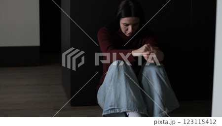 Sad woman sitting in the dark leaning against the wall in home. Domestic violence, family problems, stress, violence. 123115412