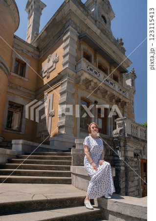 A woman is sitting on a set of stairs in front of a large building 123115413
