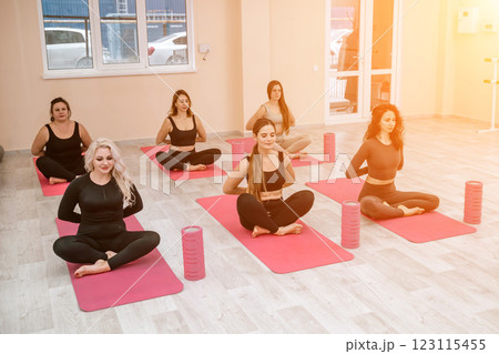 A group of six athletic women doing pilates or yoga on pink mats in front of a window in a beige loft studio interior. Teamwork, good mood and healthy lifestyle concept. A group of six athletic women doing pilates or yoga on pink mats in front of a window in a beige loft studio interior. Teamwork, good mood and healthy lifestyle concept. 123115455