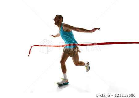 Dynamic photo of young man, runner breaking red ribbon, ultimate triumph and endurance captured in motion against white studio background. Dynamic photo of young man, runner breaking red ribbon, ultimate triumph and endurance captured in motion against white studio background. 123115686