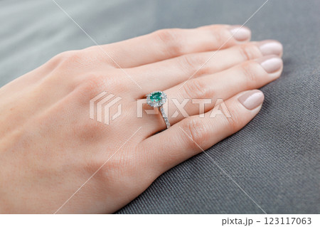 Beautiful female hand with gold ring with diamonds and emerald on gray background Beautiful female hand with gold ring with diamonds and emerald on gray background 123117063