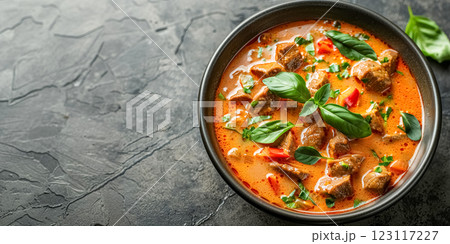 Top view of delicious bowl of spicy Thai curry with tender meat and fresh herbs on gray background with copy space 123117227